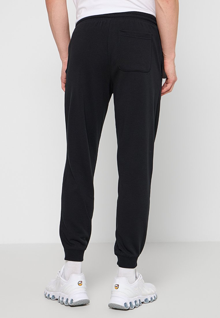 Pantaloni jogger neri con vita elastica, polsini affusolati e una tasca posteriore, realizzati in materiale morbido. Indossati con scarpe da ginnastica bianche.