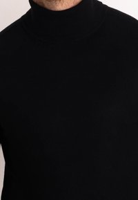 Czarny golf wykonany z gładkiej, elastycznej tkaniny; posiada dopasowany krój i prążkowaną teksturę przy kołnierzu.