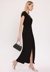 Czarna sukienka do kolan z krótkimi rękawami i głębokim dekoltem w kształcie litery V, z bocznym rozcięciem. Połączona ze srebrnymi sandałami na obcasie i koralikową kopertówką.
