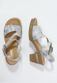 Sandaalit, joissa on kukkakuosiset vaaleansiniset ylämateriaalit, korkkimaisen tekstuurin omaava korko ja säädettävä nilkkastrap. Pehmeä pohja näkyvissä.