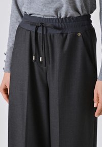 Pantaloni neri a gamba larga con vita elasticizzata e coulisse, abbinati a un top grigio a maniche lunghe con dettagli a bottoni sulle maniche.