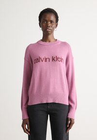 Maglione rosa a maglia con colletto rotondo, con la scritta "calvin klein" in un rosa più scuro. Maniche lunghe e vestibilità comoda. Texture morbida.