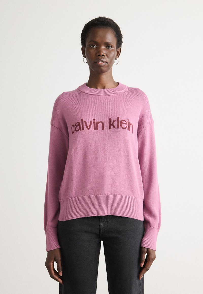 Maglione rosa a maglia con colletto rotondo, con la scritta "calvin klein" in un rosa più scuro. Maniche lunghe e vestibilità comoda. Texture morbida.
