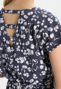 Dunkelblaues Blumenkleid mit kurzen Ärmeln, elastischem Bund und Rückenausschnitt mit drei horizontalen Stoffstreifen.