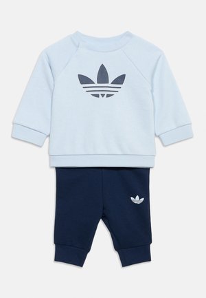 Světle modrá mikina s dlouhými rukávy s tmavě modrým logem Adidas, doplněná tmavě modrými kalhotami s malým bílým logem Adidas na nohavici.