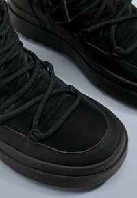 Czarne buty z teksturowanym wierzchem, grubymi sznurówkami i masywną podeszwą. Projekt zawiera gładkie wykończenie i wzmocnione szwy.