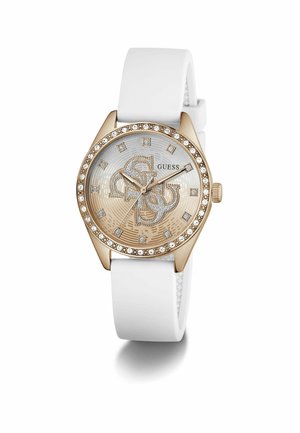 Ceas cu ton auriu, curea din silicon alb, carcasă rotundă, accente cristale și cadran cu model care prezintă un logo stilizat și marcaje pentru ore.