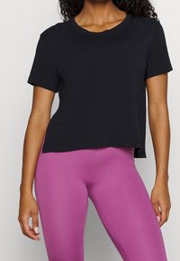 Camiseta negra de manga corta con cuello redondo, fabricada con tela suave, combinada con leggings ajustados de color rosa, textura lisa, diseño minimalista.
