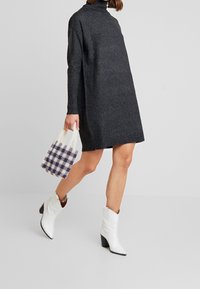 Robe en maille grise à col montant, associée à des bottes cowboy blanches. Accessoirisée d'un petit sac à carreaux violet et crème.