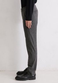 Gray wool trousers with a relaxed fit, elastic waistband, and side pockets. Worn with black lace-up shoes, showcasing a slim silhouette.