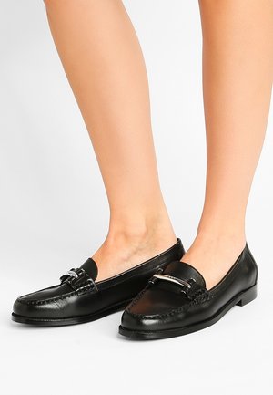 Mocassins en cuir noir avec une semelle plate, dotées d'un accent en métal argenté et de détails cousus autour des orteils et des côtés.