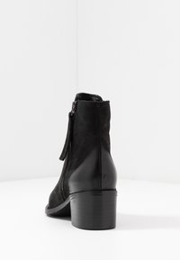 Stivale alla caviglia in suede nero con tacco lucido, chiusura a cerniera laterale e texture liscia, caratterizzato da un design con tacco alto e affusolato.