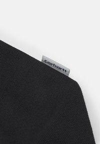 Tissu de toile noire avec une surface texturée, présentant une petite étiquette grise avec le texte "carhartt" le long du bord.