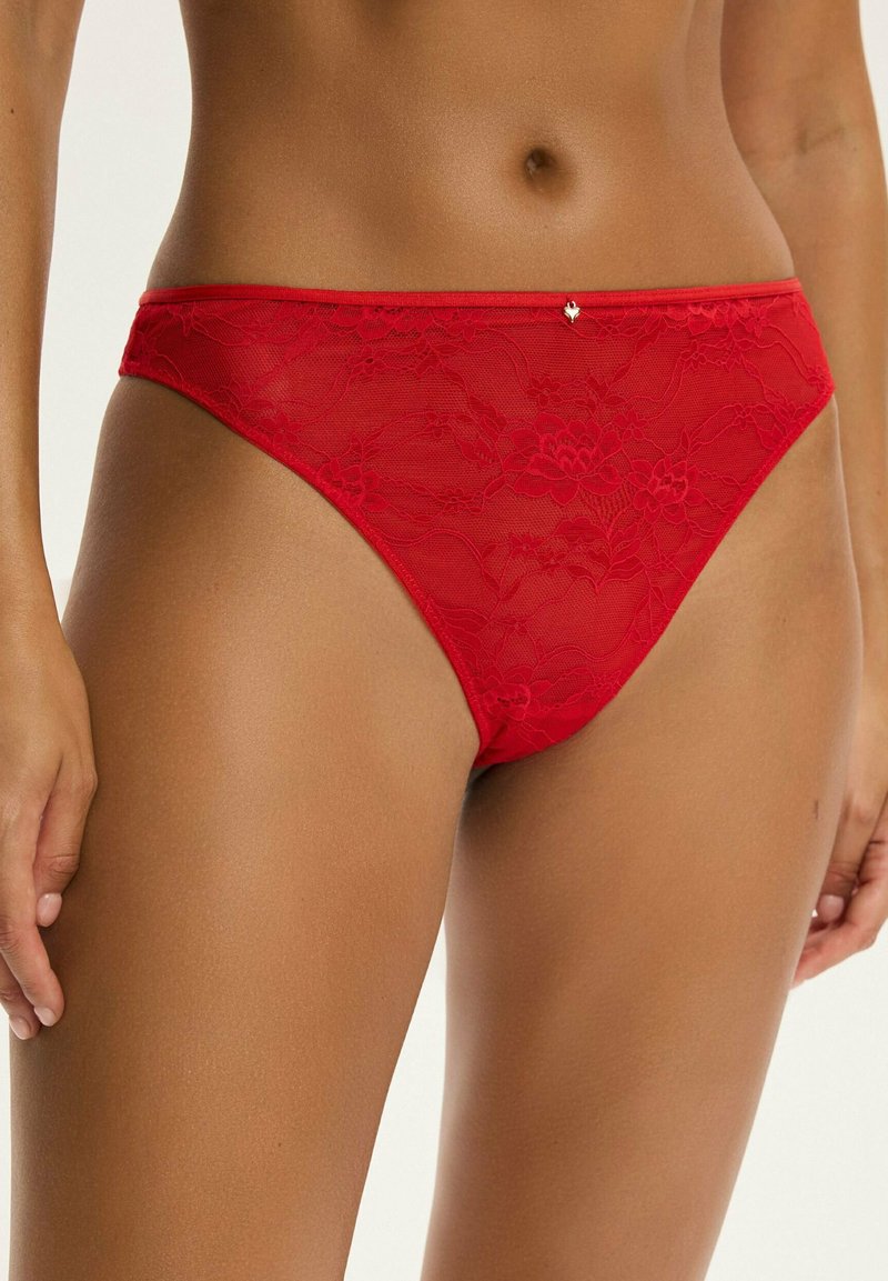 Czerwony koronkowy string z kwiatowymi wzorami, gładką teksturą, wąskimi bocznymi paskami i małym ozdobnym detalem w talii.