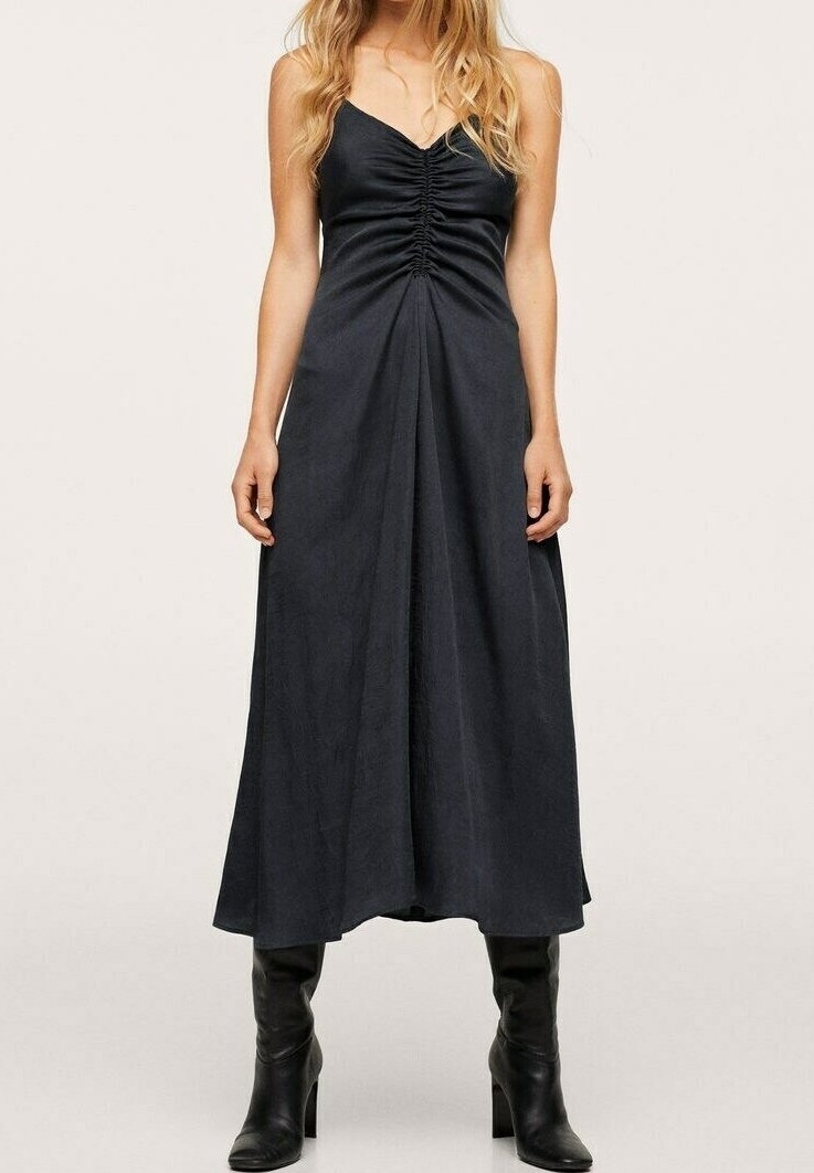 Musta maksimekko, jossa on V-niska ja rypytys rinnassa, virtaava siluetti, valmistettu sileästä kankaasta. Yhdistetty polveen ulottuviin mustiin saappaisiin.