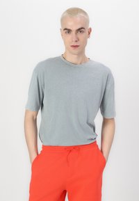 Maglietta di cotone grigia con scollo rotondo e maniche corte, abbinata a pantaloni corti arancioni con coulisse, su uno sfondo bianco.