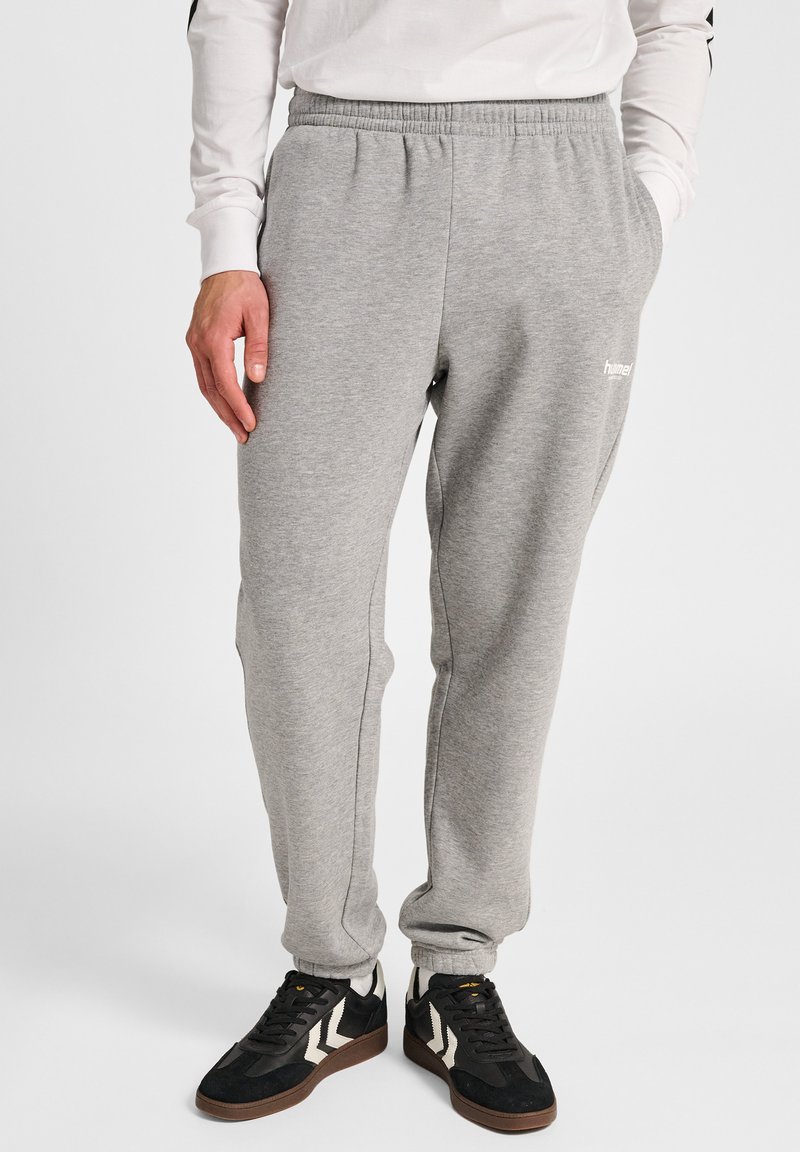 Grijze sweatpants met een elastische tailleband, zijzakken en logodetail. Gecombineerd met zwarte sneakers met een gestreept ontwerp.