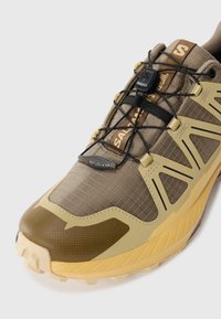 Brown and yellow Salomon trail running shoe with quick-lace system and textured sole for off-road grip.