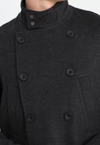 Zwart wollen double-breasted jas met een hoge kraag, voorzien van grote zwarte knopen, textuurstof en een voorzak.