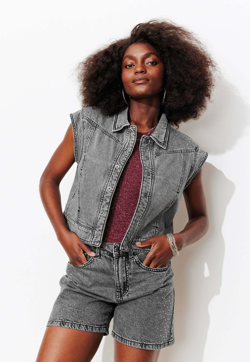 Veste en jean gris à manches courtes, ornée de clous métalliques. Associée à un short gris assorti et un haut texturé bordeaux.