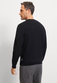 Zwarte gebreide trui met een ronde hals en lange mouwen, met een zijaccent met blauwe en witte details aan de zoom. Gladde textuur.