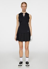 Black sleeveless polo top with a white accent collar, paired with a pleated black skirt. Worn with black and white sneakers and a white glove.