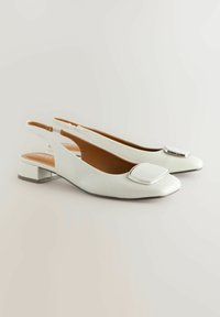 Ballerines blanches en cuir avec un bout carré et un accent argenté sur le dessus. Talon bas et design à talon ouvert pour un enfilage facile.