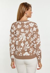 Pulover tricotat maron cu model floral alb, guler rotund și mâneci lungi. Cuff-uri și tiv ribbate. Purta peste pantaloni albi.