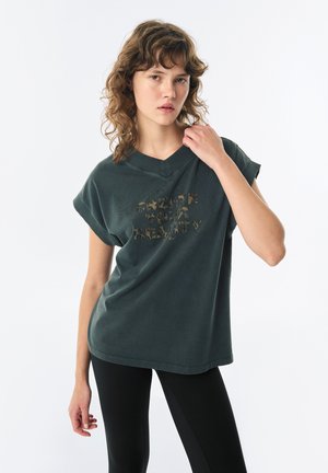Dunkelgrünes Baumwoll-T-Shirt mit V-Ausschnitt, hochgerollten Ärmeln und einem Leopardenmuster-Textgrafik mit dem Schriftzug "GESTALTE DEINE REALITÄT."