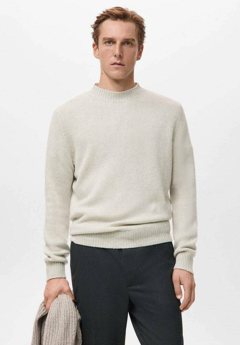 Pull en maille gris clair avec un col rond côtelé et des manches longues, présentant une coupe décontractée. Le modèle tient un châle beige texturé.