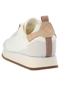 White sneaker with a textured fabric upper, beige suede accents, and a brown pull tab. Features a white midsole and a rubber outsole.