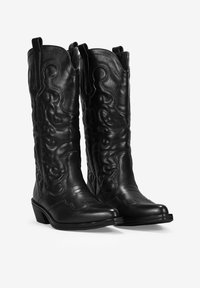 Botas de cowboy de cuero negro con intrincados bordados en relieve, punteras puntiagudas y lengüetas. Presentan un tacón bajo apilado y un patrón texturizado.