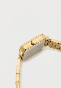 Kultainen suorakulmainen kello, jossa on teksturoitu hopeadiialli, korostunut kruunu ja linkitetyllä metallirannekkeella varustettu, jossa on tasaisesti järjestettyjä suorakulmaisia linkkejä.