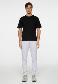 T-shirt en coton noir à manches courtes, associé à un pantalon de survêtement gris clair en tissu doux, avec des poignets élastiques et une taille à cordon de serrage.