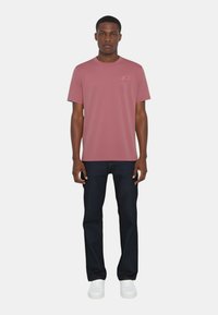 T-shirt rosa a girocollo in cotone, con maniche corte e un piccolo logo ricamato. Abbinato a jeans scuri in denim e sneakers bianche.