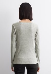 Maglietta verde chiaro a maniche lunghe con motivo a costine testurizzate, scollo arrotondato e silhouette aderente, abbinata a jeans scuri.