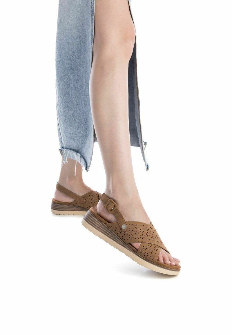 Sandalias de cuero perforadas en marrón con un diseño de talón abierto, que cuentan con una correa con hebilla y una suela texturizada en beige para un mejor agarre.