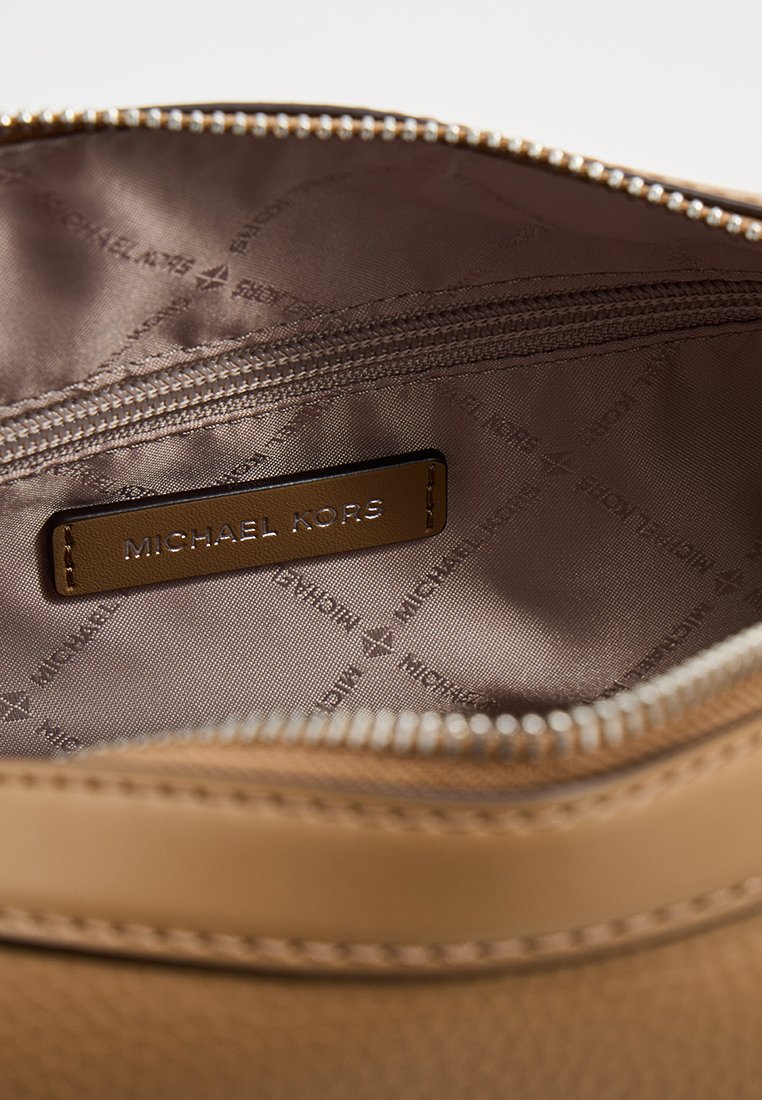 Intérieur synthétique marron d'un sac à main avec fermeture éclair, présentant une étiquette en cuir estampillée "MICHAEL KORS" et un doublage avec motif de logo.