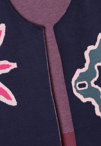 Námořnická pletená oděv s růžovými květinovými a tyrkysovými abstraktními vzory. Obsahuje kulatý výstřih a texturovaný růžový akcent.