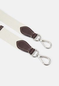 Beżowy pasek z płótna z brązowymi skórzanymi akcentami, wyposażony w srebrne metalowe okucia i zapięcia zatrzaskowe do mocowania. Wytrzymała i funkcjonalna konstrukcja.