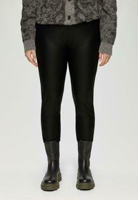 Zwarte faux leren leggings met een aansluitend ontwerp, voorzien van een gladde textuur en een cropped lengte, gecombineerd met zwarte laarzen en een grijze cardigan.