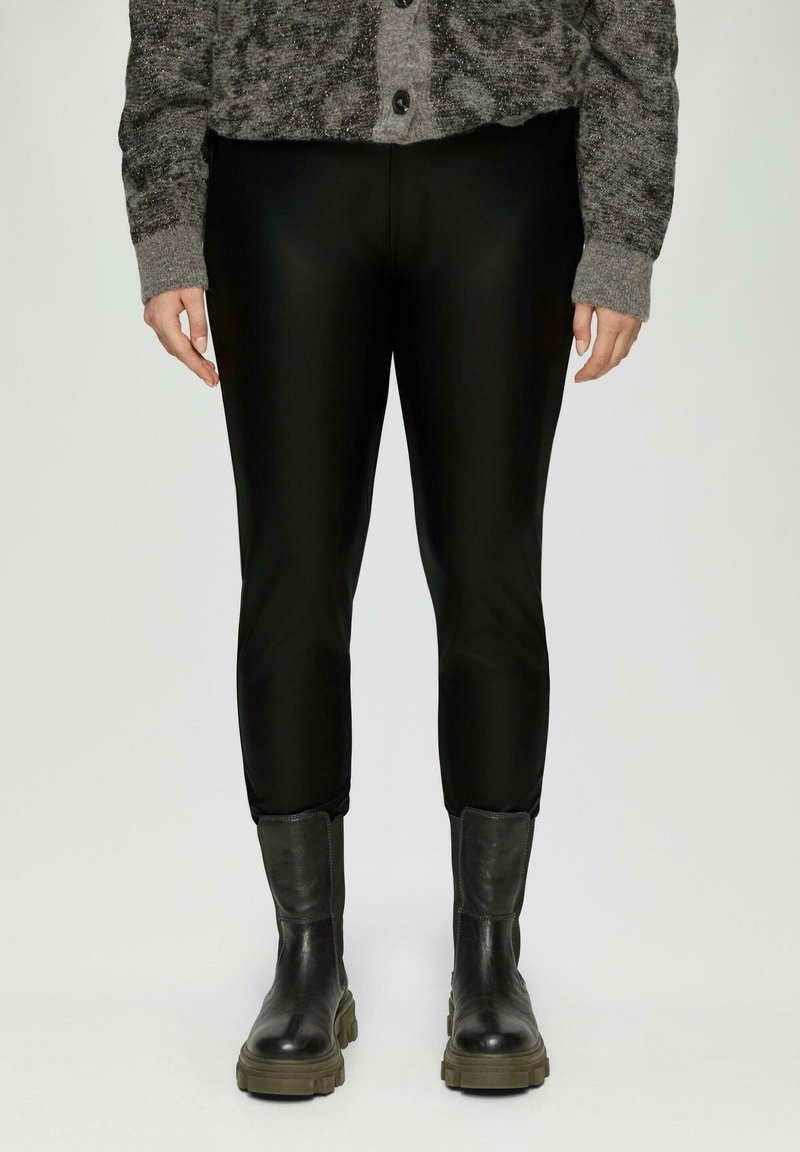 Zwarte faux leren leggings met een aansluitend ontwerp, voorzien van een gladde textuur en een cropped lengte, gecombineerd met zwarte laarzen en een grijze cardigan.