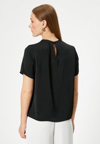 Sort kort�ærmet bluse med rund hals og en lille nøglehulskæring bagpå, med en glat tekstur og afslappet pasform.