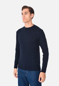 Pullover lavorato a maglia blu navy con un motivo a nido d'ape testurizzato, colletto rotondo e polsini a coste, abbinato a jeans blu scuro.