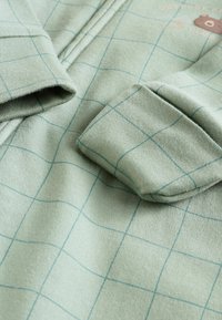 Pull vert avec un motif en grille de lignes bleu clair, présentant une texture douce et un patch d'ours en accent sur la poitrine.