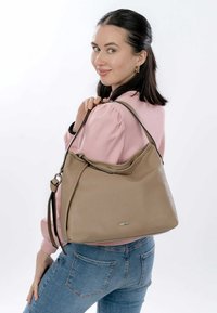 Beige perforated leather handbag with a slouchy design, dual handles, and a subtle logo accent. Worn over the shoulder against a light background.