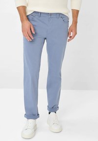 Chino in cotone blu chiaro con una vestibilità slim, dotati di risvolti, due tasche frontali e chiusura con bottone. Abbinati a sneakers bianche.