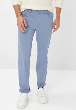 Chinos en coton bleu clair avec une coupe slim, dotés de revers roulés, de deux poches avant et d'une fermeture à bouton. Associés à des baskets blanches.