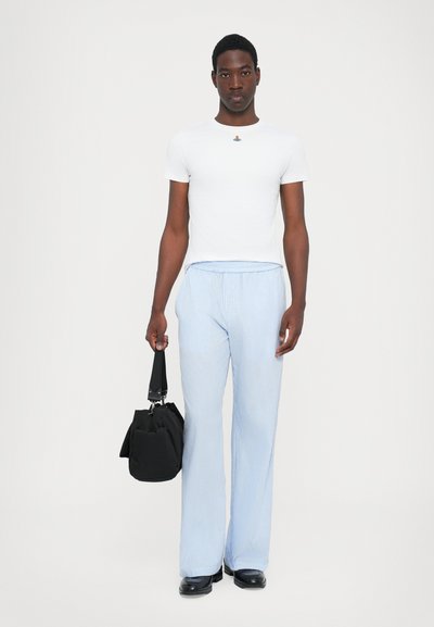T-shirt ajusté blanc avec un petit logo coloré, pantalon large rayé bleu et blanc, tenant un sac noir à anse courte.