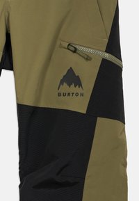 Lyžařské kalhoty s zúženým střihem, vyrobené z olivově zeleného a černého materiálu, s kapsou na zip a logem hory.